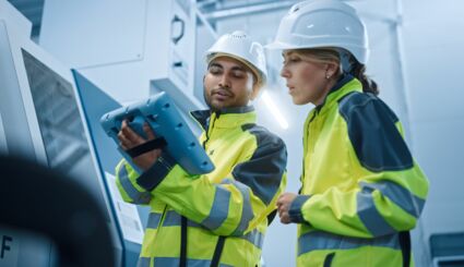 Eine Frau und ein Mann mit Sicherheitskleidung kontrollieren ein Werk