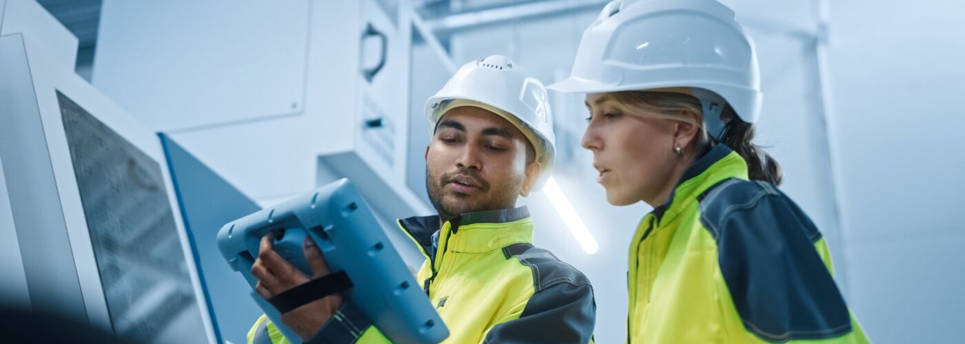 Eine Frau und ein Mann mit Sicherheitskleidung kontrollieren ein Werk