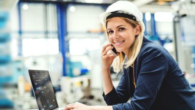 Geprüfte Industriemeisterin in Werkstatt telefoniert vor Laptop